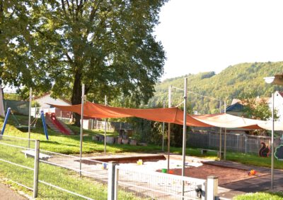 Außengelände der Krippe mit Sonnensegel, Sandkasten und Bäumen