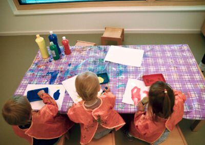 Kinder in Malkitteln malen von hinten gesehen am Tisch mit Farben